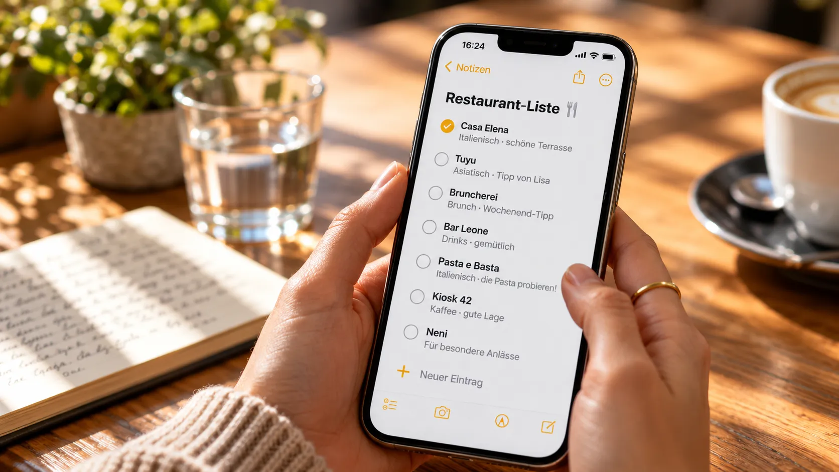 Smartphone mit einer Restaurantliste in einer Notizen-App, gehalten über einem Café-Tisch